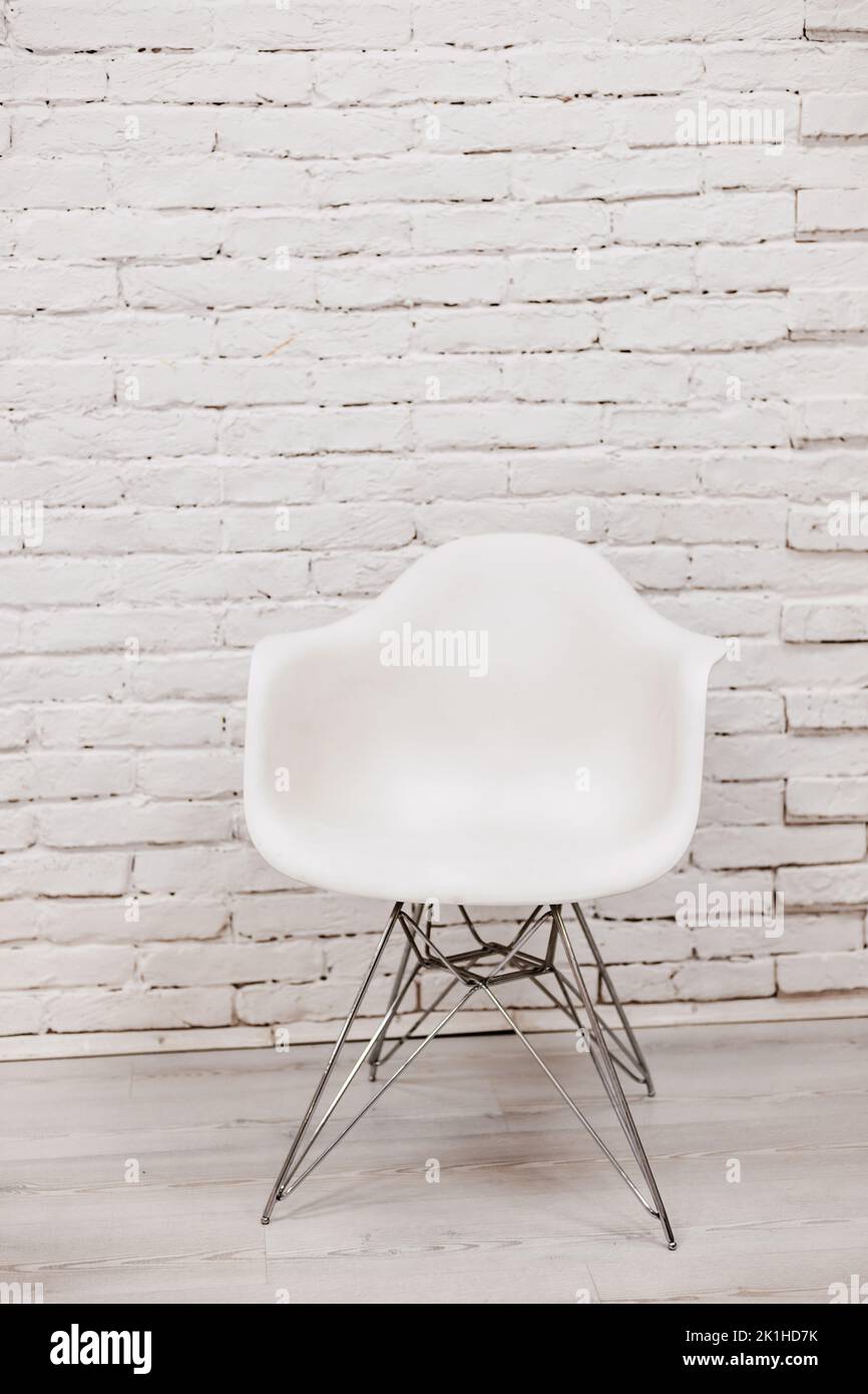 Una moderna sedia bianca si erge vicino ad una parete di mattoni bianchi. Foto Stock