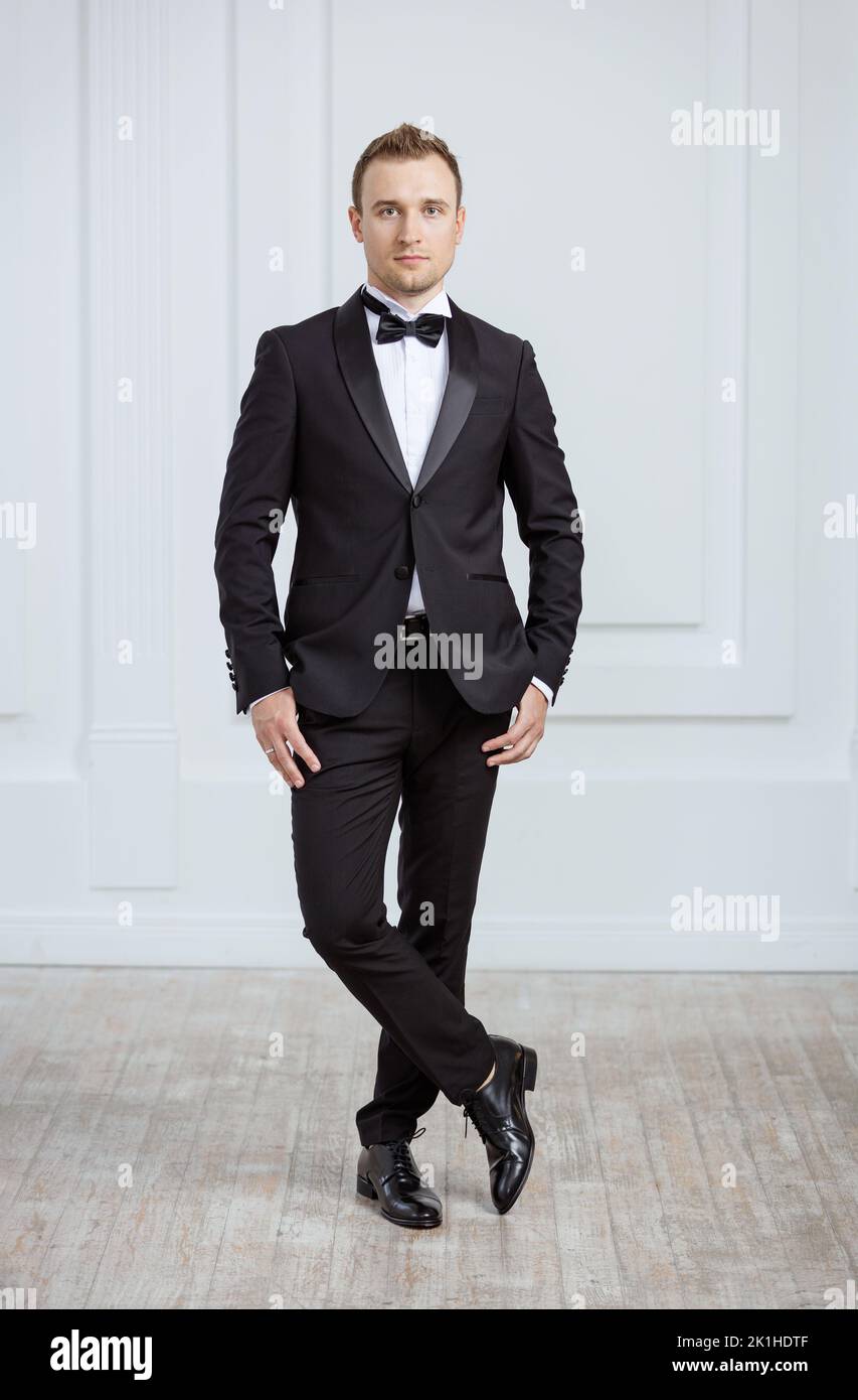 Attraente giovane uomo in piedi in tuxedo in interni e guardando la macchina fotografica Foto Stock