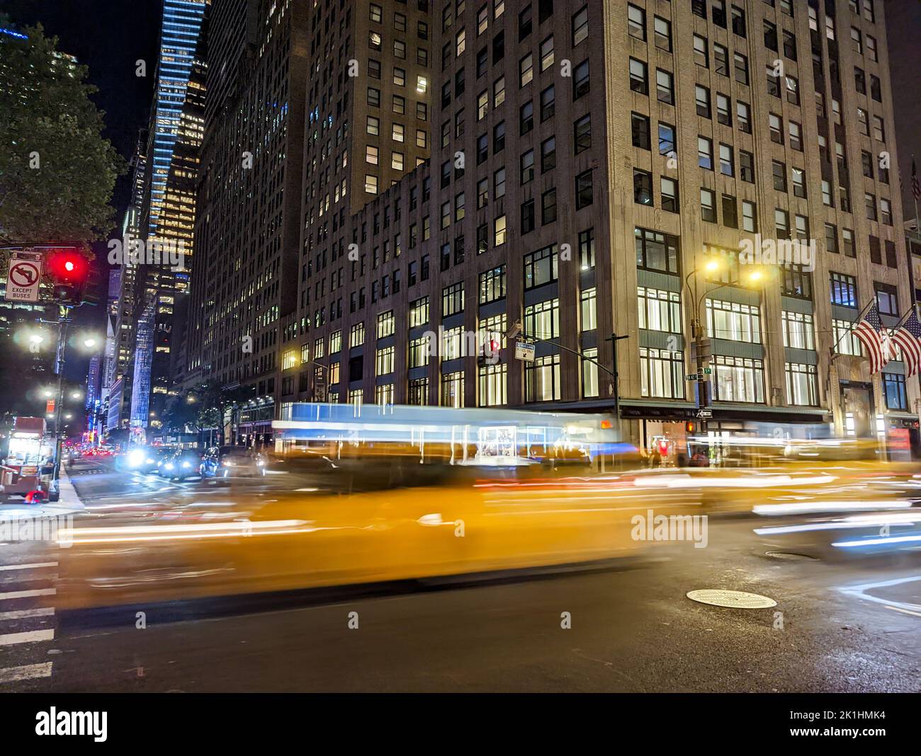 Movimento sfocato di un taxi giallo che guida lungo la strada attraverso New York City di notte con le luci dell'edificio sullo sfondo Foto Stock