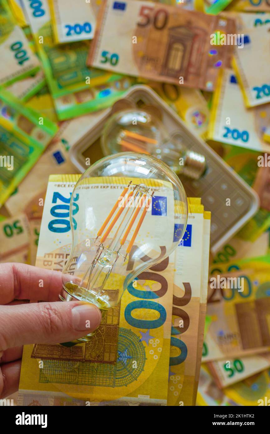 Costo dell'elettricità in Europa. Lampadina in mano su sfondo bollette in euro. Aumento dei prezzi dell'elettricità. Pagamento per servizi di utilità. Produzione di energia Foto Stock