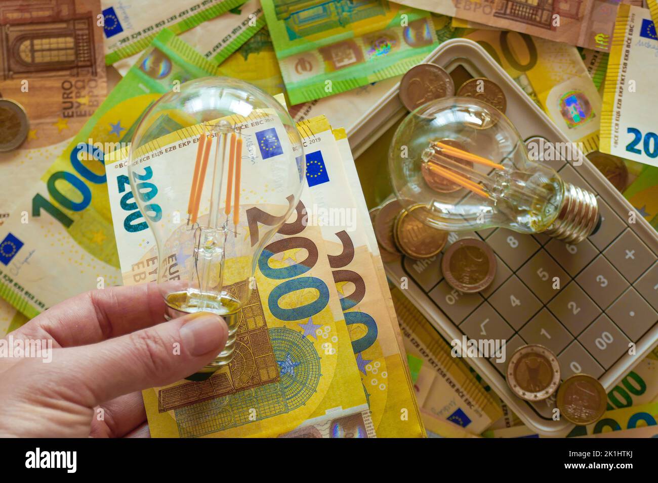 Lampadina elettrica in mano sullo sfondo delle banconote in euro. Aumento dei prezzi dell'elettricità.pagare bollette elettriche.crisi della produzione di energia Foto Stock