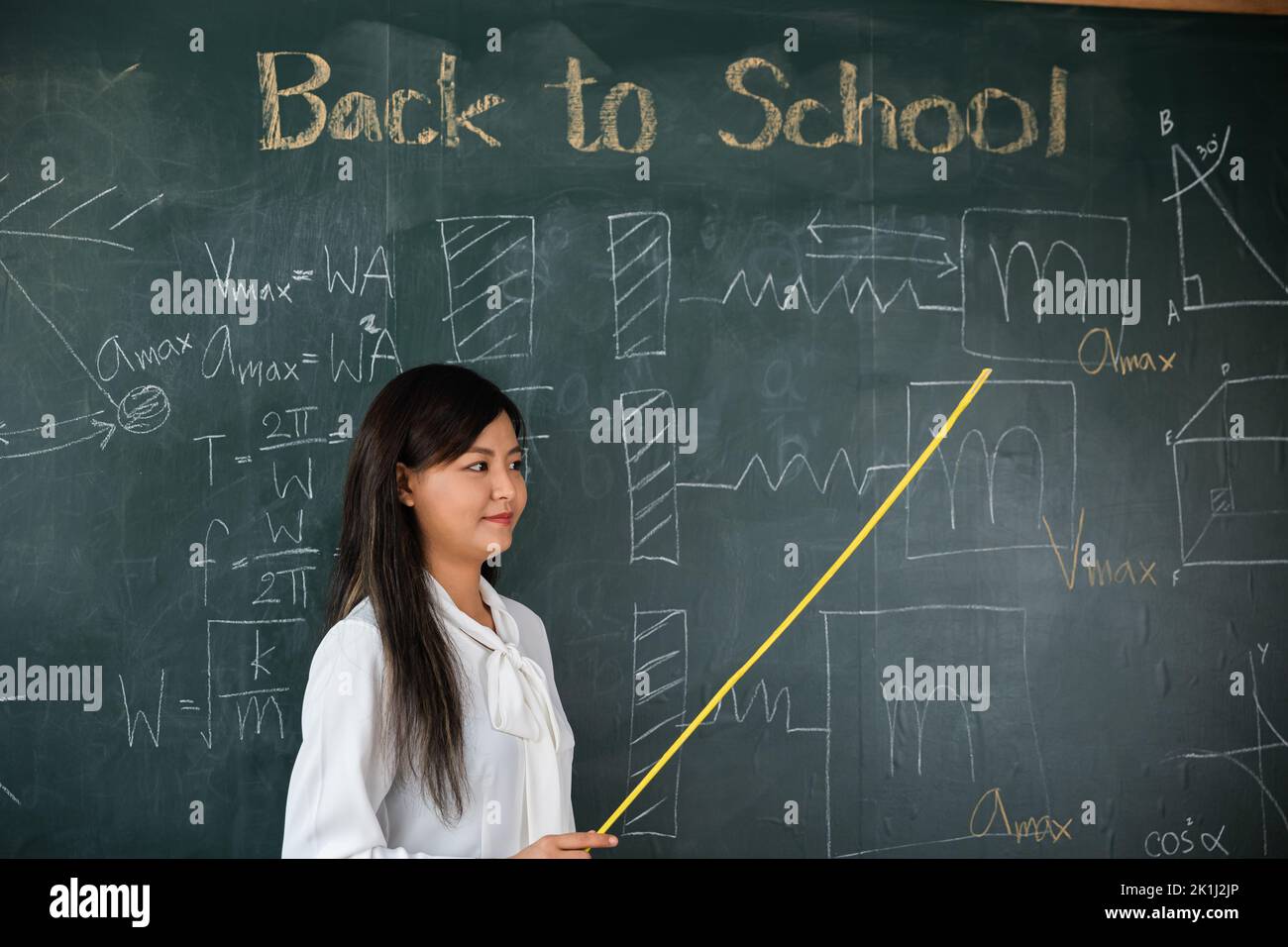 Concetto di ritorno a scuola. Insegnante femminile asiatica sorridente con bastone di legno che punta alla lavagna a scuola in classe, felice bella donna stan Foto Stock