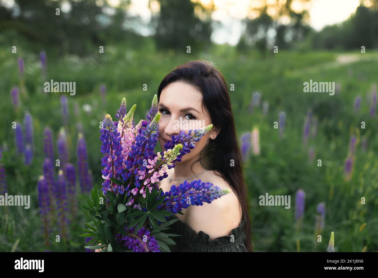Una donna attraente in un campo con un bouquet estivo di fiori selvatici Lupinus. Vista frontale. Foto Stock