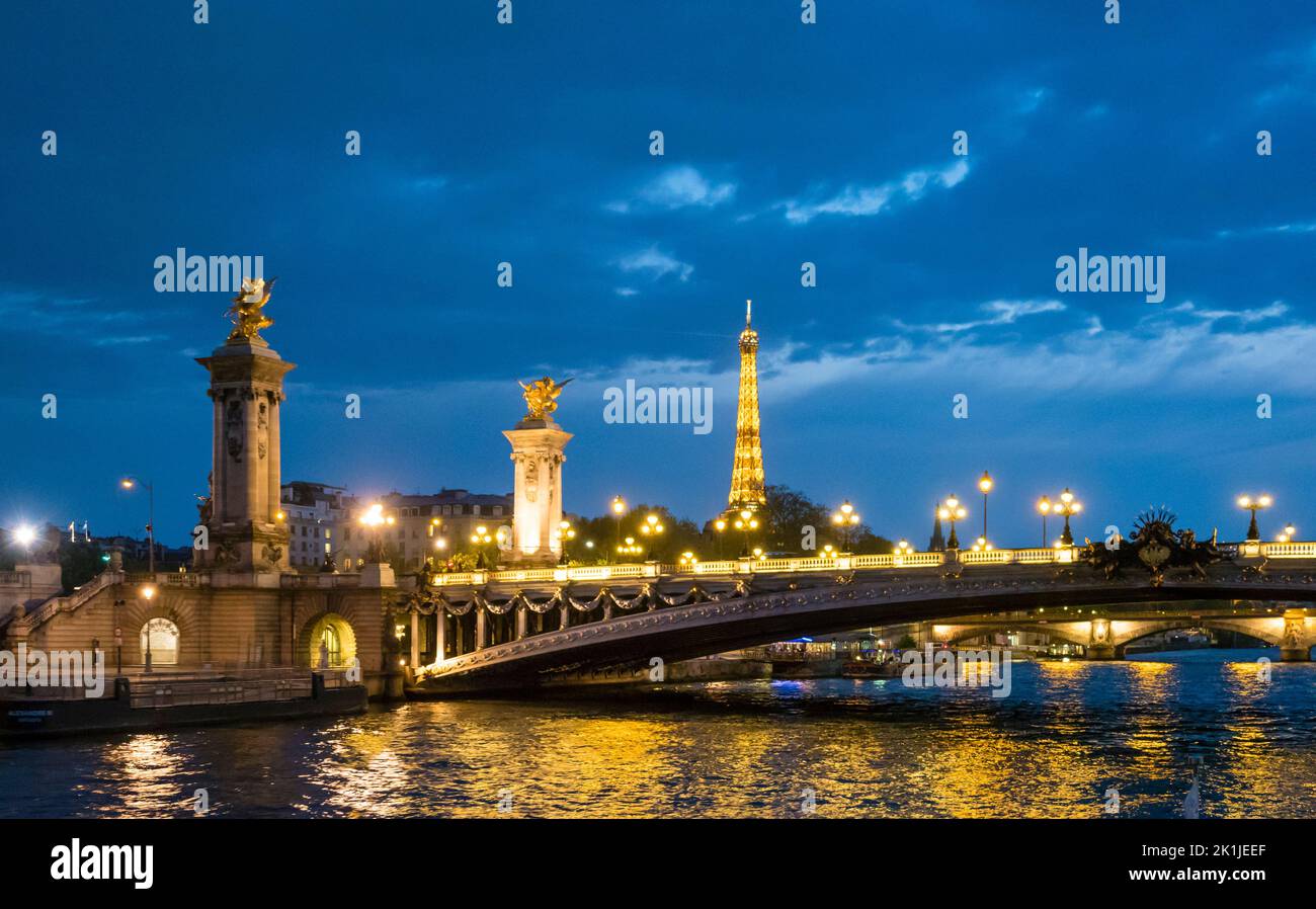 Parigi, Francia - 19 aprile 2022: Torre Eiffel illuminata e Pont Alexandre III, visto dal fiume Senna di notte Foto Stock