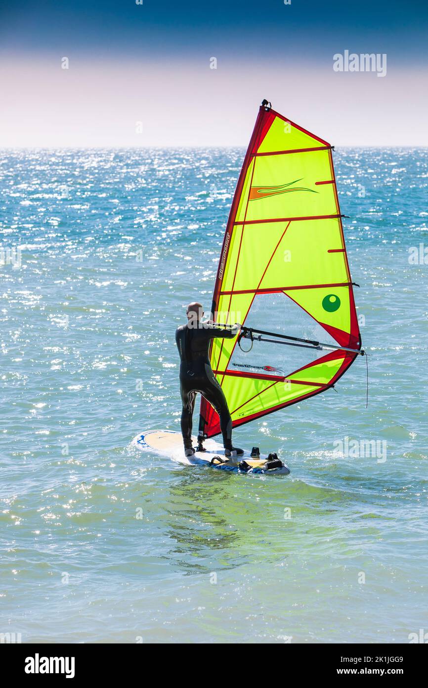 Un wind surf con una vela verde brillante su un mare blu increspato. Foto Stock