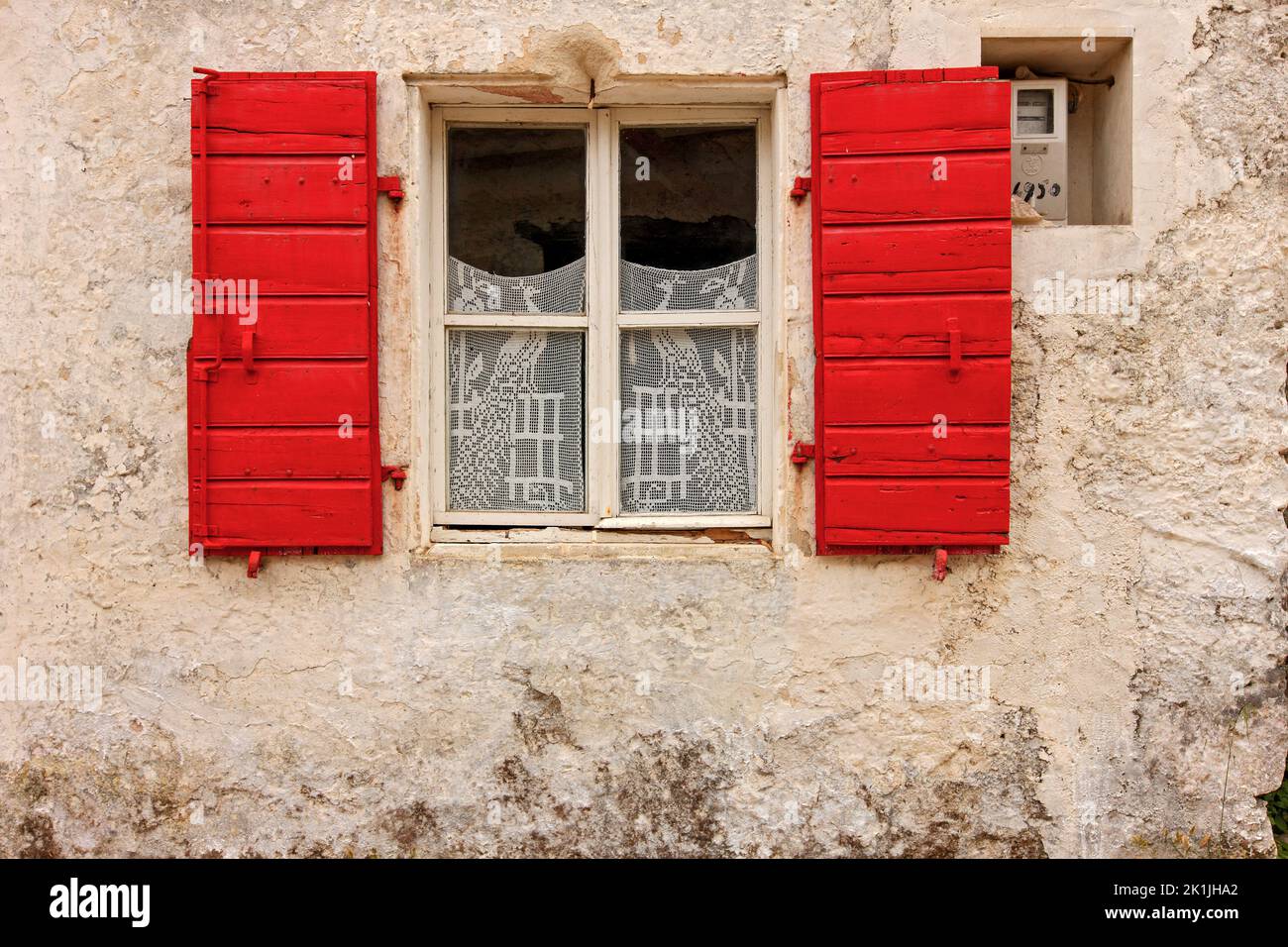 Pittoresca facciata di casa tradizionale locale con pareti in pietra, finestra rossa ed elaborate tende in pizzo, vista in un villaggio dell'isola di Zante, in Grecia Foto Stock