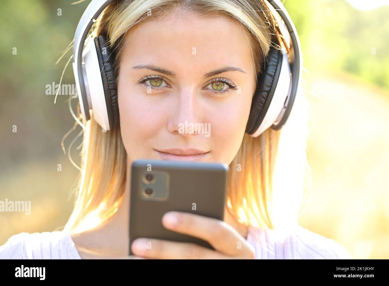 Immagine frontale di una donna che indossa cuffie wireless con uno smartphone che ti guarda Foto Stock