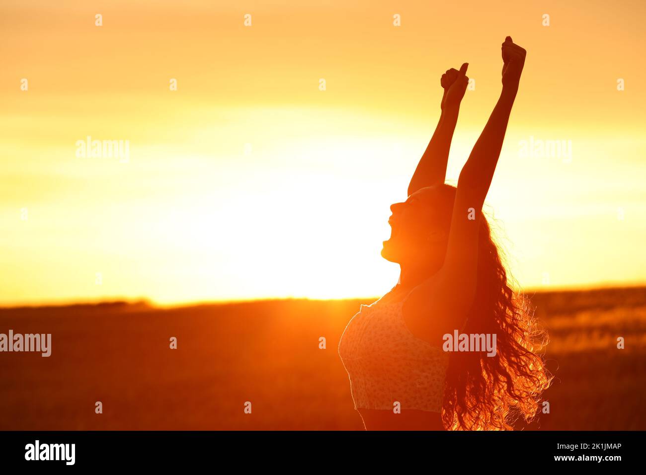 La silhouette di una donna eccitata che alza le braccia al tramonto festeggia Foto Stock
