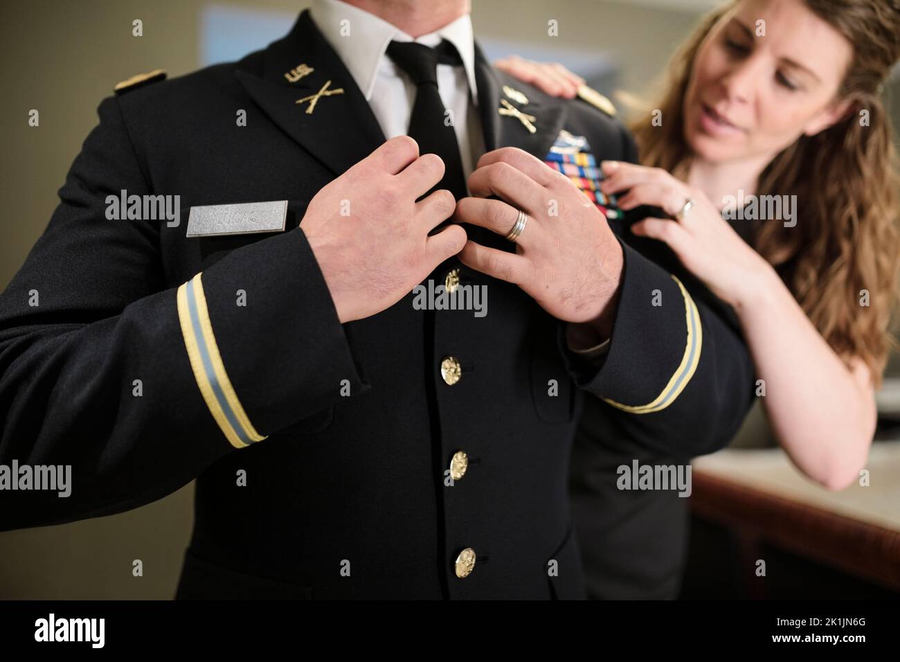 Moglie che aiuta marito con abito militare uniforme Foto Stock