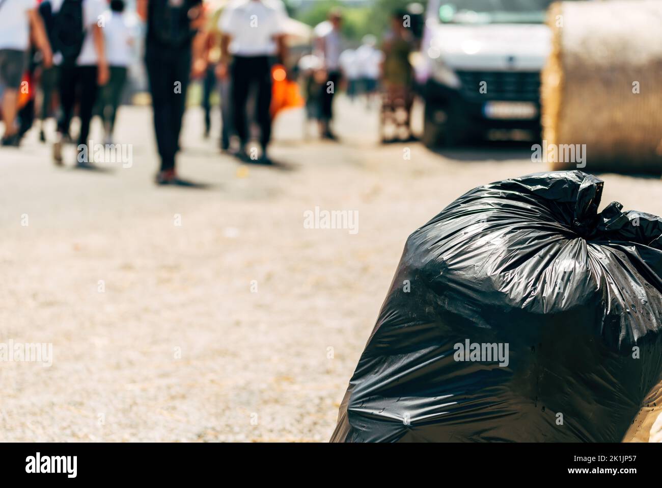 Lettering e inquinamento in città, sacchetto di spazzatura nero sulla strada con persone pedoni a piedi, fuoco selettivo Foto Stock