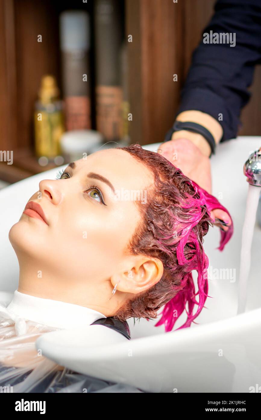 Lavaggio capelli tinti femmina. Una giovane donna caucasica che ha i capelli lavati in un salone di bellezza. Il parrucchiere professionale lava la vernice di colore rosa dai capelli di un cliente Foto Stock