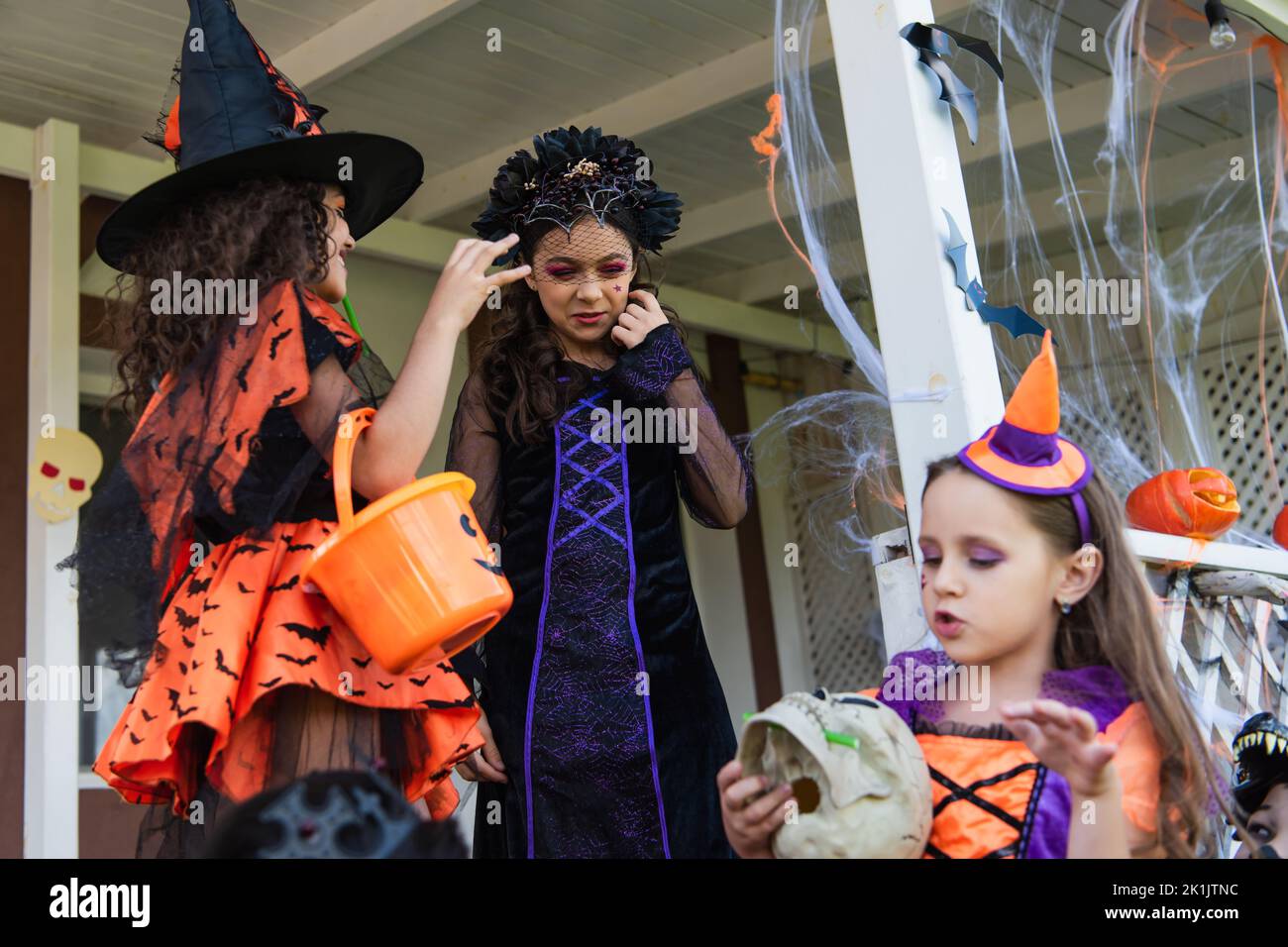 ragazze in costumi di halloween che detengono cranio e trucco o secchio trattare vicino a cottage decorato Foto Stock