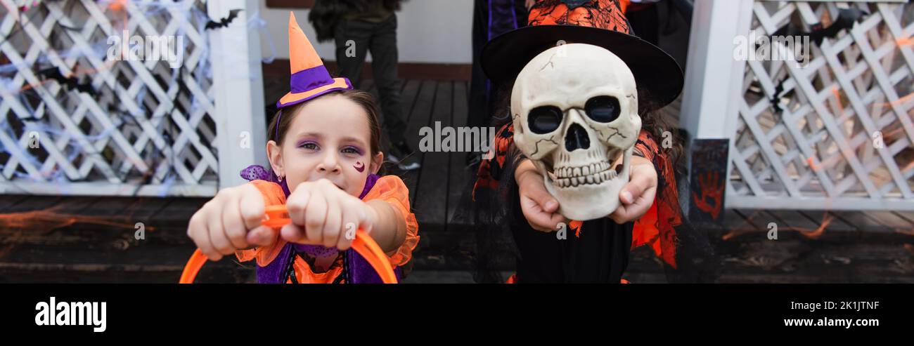 ragazza volto oscuro con cranio spettrale vicino amico in costume clown, banner Foto Stock