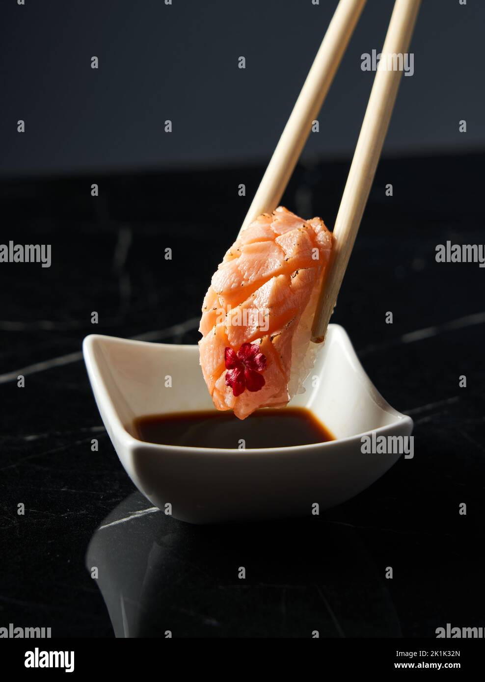 Primo piano mano che tiene bacchette di bambù con nigiri di salmone mentre si immerge a mano nigiri in salsa di soia al ristorante. Vista frontale. Cibo, cucina giapponese c Foto Stock