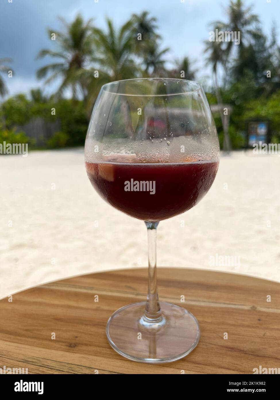 Un bicchiere di sangria servito sulla spiaggia in un lungo bicchiere di vino su un'isola delle Maldive. Messa a fuoco selettiva sul vetro. Foto Stock