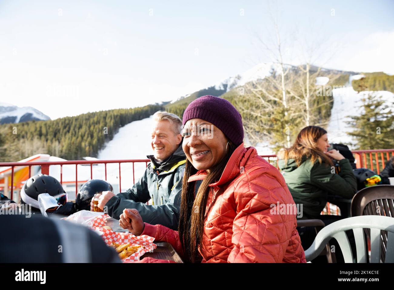 Felice sciatore femmina che si gode il pranzo con gli amici sul patio soleggiato della stazione sciistica Foto Stock
