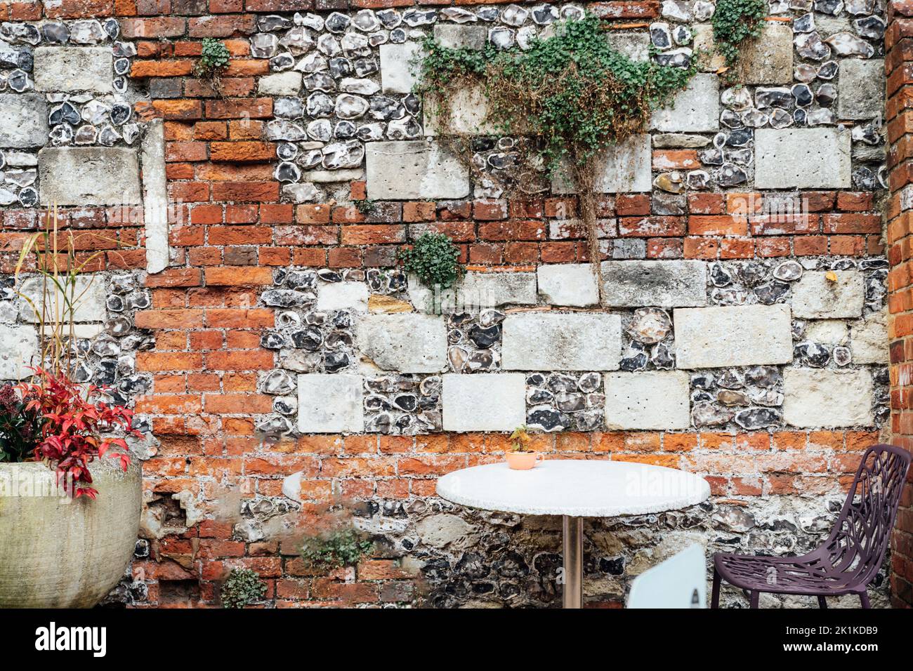 Tavolo da caffe' in pietra e sedia moderna vicino al vecchio muro di mattoni e pietra con vegetazione crescente. Caffè della città vecchia con un'atmosfera vintage. Messa a fuoco selettiva, copia sp Foto Stock