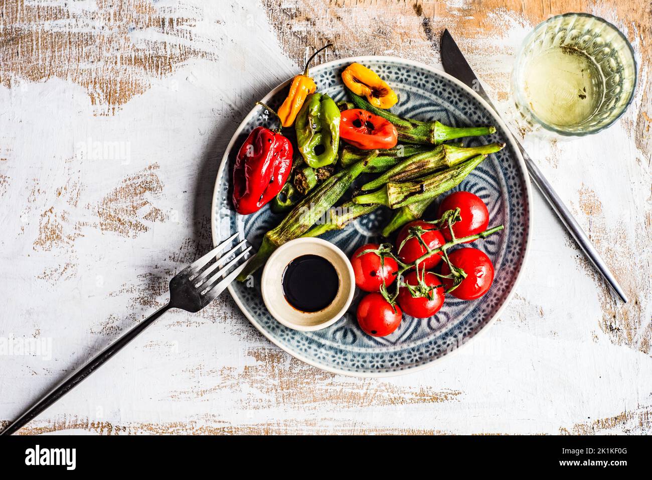 Piatto di okra arrosto, pomodori e peperoni con condimento balsamico di soia e un bicchiere di vino bianco Foto Stock