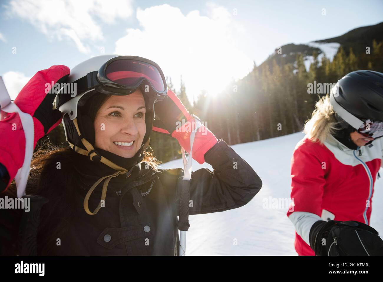 Ritratto sorridente sciatore femmina che regola il casco sulle piste da sci innevate e soleggiate Foto Stock