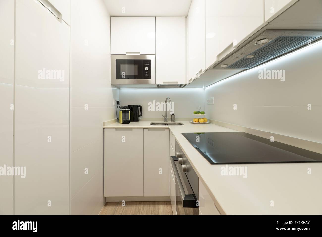Piccola cucina con semplici armadi bianchi, abbinati piani in pietra e elettrodomestici da incasso Foto Stock