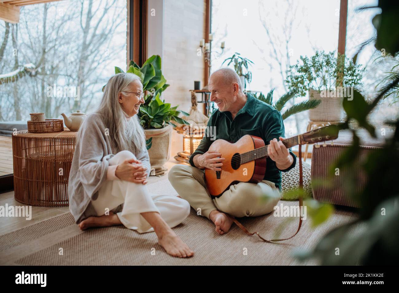 Uomo anziano che suona in chitarra sua moglie, seduto in un accogliente salotto e godersi la giornata autunnale. Foto Stock