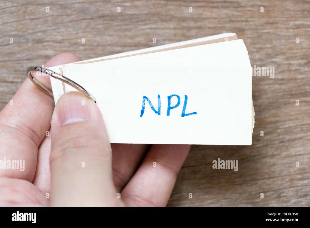 Scheda flash di tenuta della mano con scrittura a mano in parola NPL (abbreviazione di prestito non performante, letteratura non brevettuale) su fondo di legno Foto Stock