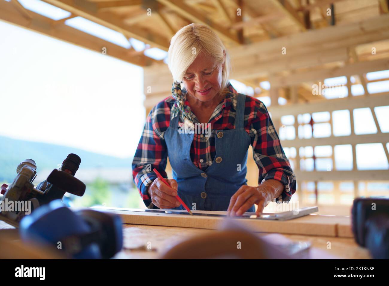 Donna anziana manuale di lavoro all'interno della sua casa ecologica sostenibile in legno incompiuta. Concetto di donne e anziani indipendenti attivi, eco Foto Stock