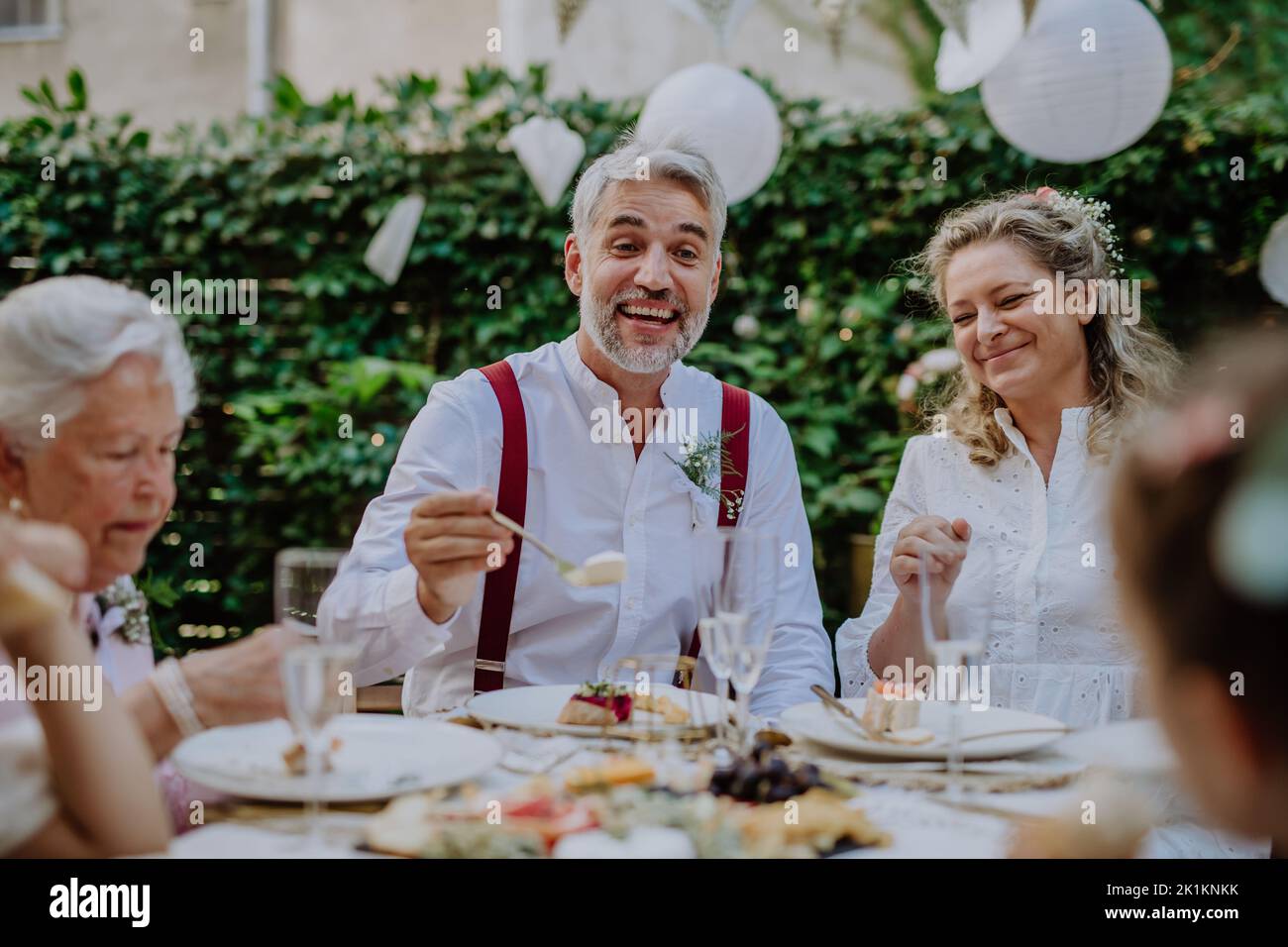 Sposa matura e sposi con gli ospiti al ricevimento di nozze all'esterno nel cortile. Foto Stock