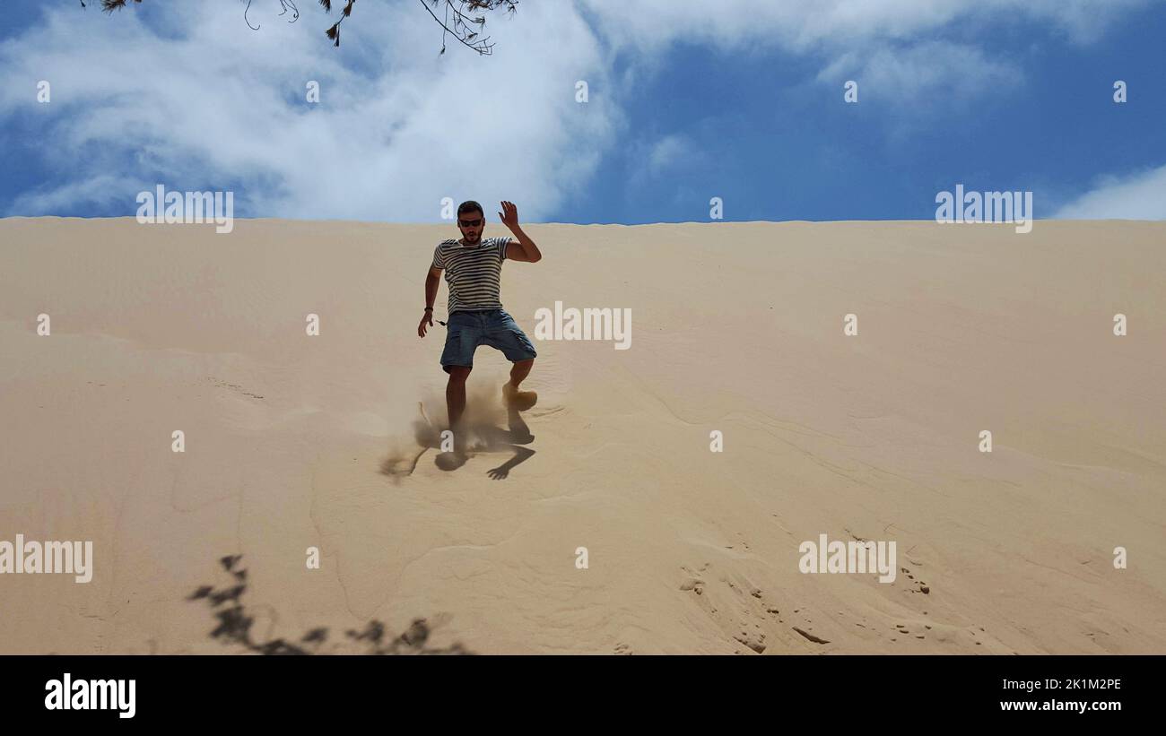 Un uomo che corre, saltando e divertendosi tra le dune. Foto Stock