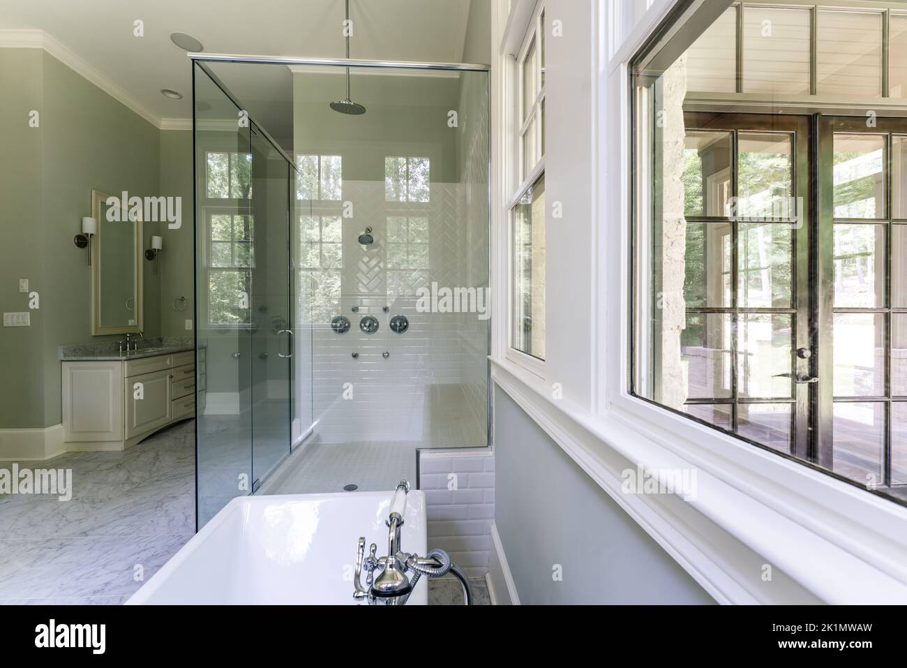 Bagno verde salvia con finiture bianche dover, vasca indipendente, doccia chiusa con vetro con mattoni a spina di pesce dipinti in bianco, piano di granito Foto Stock