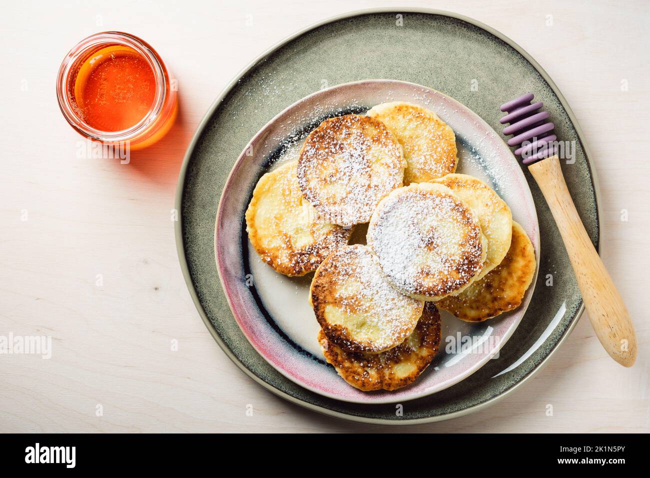 Pancake al formaggio casolare con miele su sfondo di legno chiaro, vista dall'alto. Foto Stock