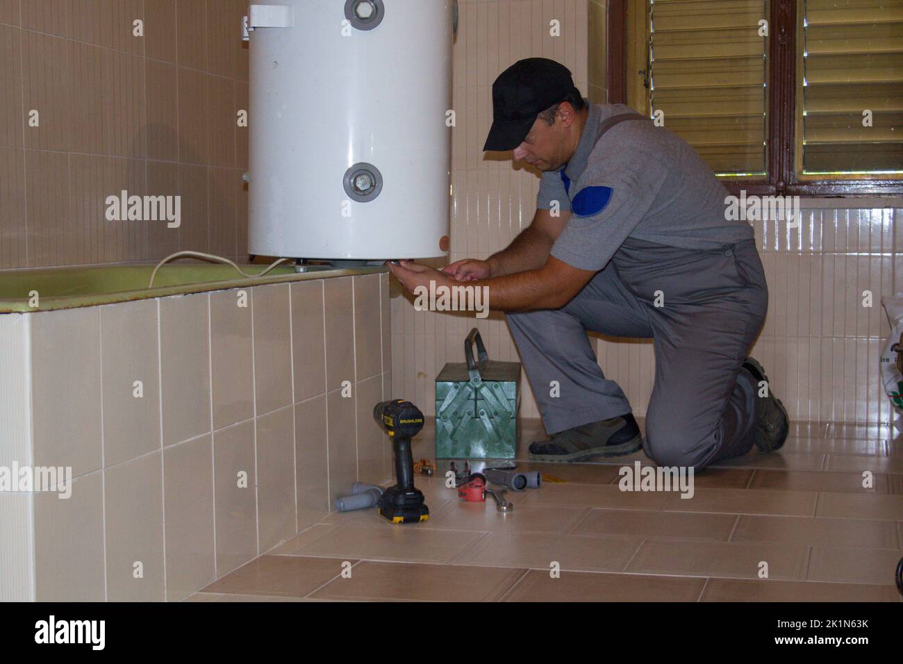 Idraulico in bagno di una casa che con i suoi attrezzi di lavoro ripara un scaldabagno elettrico. Installazione di una caldaia in bagno, fai da te Foto Stock