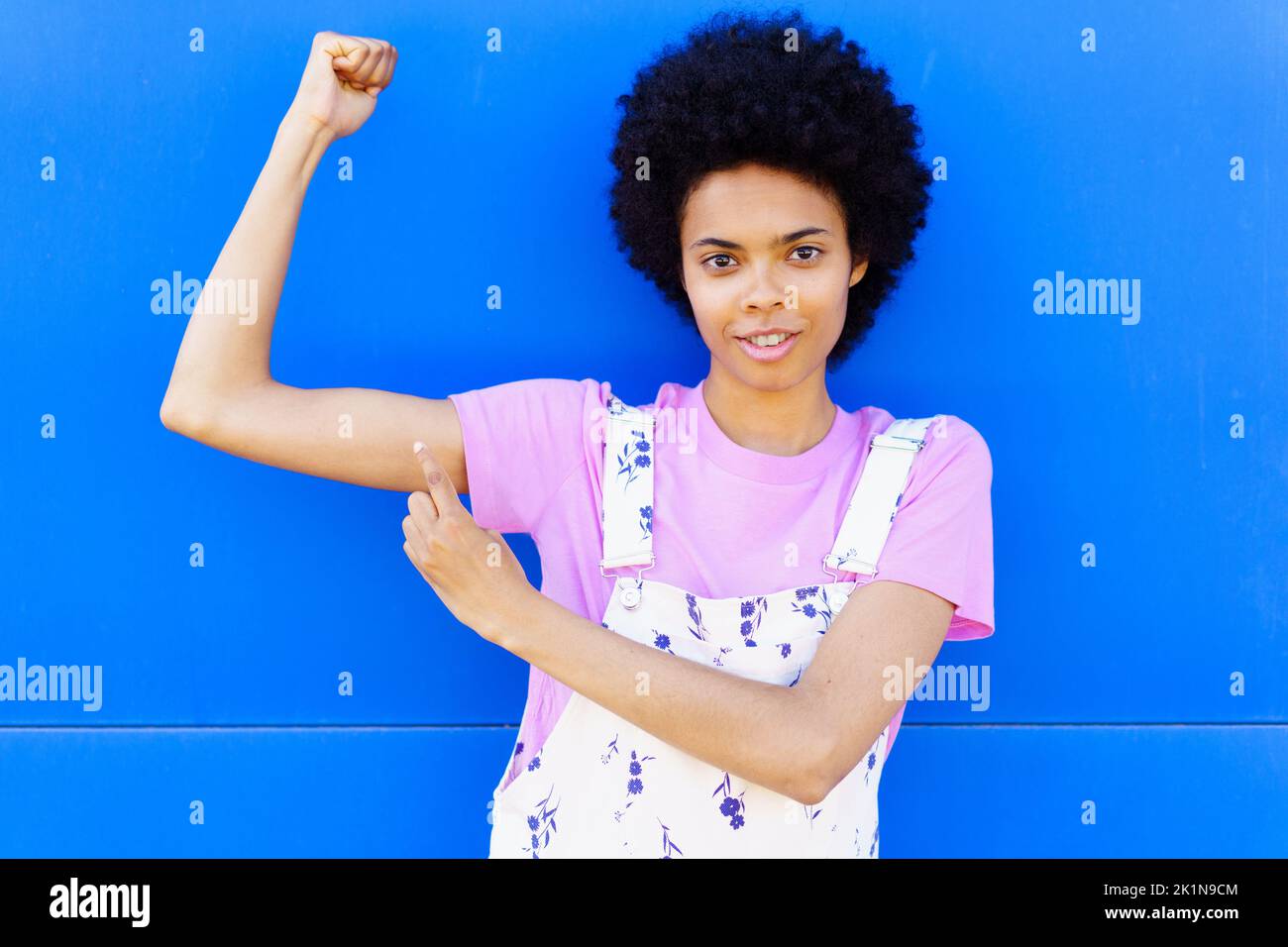 Donna nera che mostra i muscoli vicino alla parete blu Foto Stock