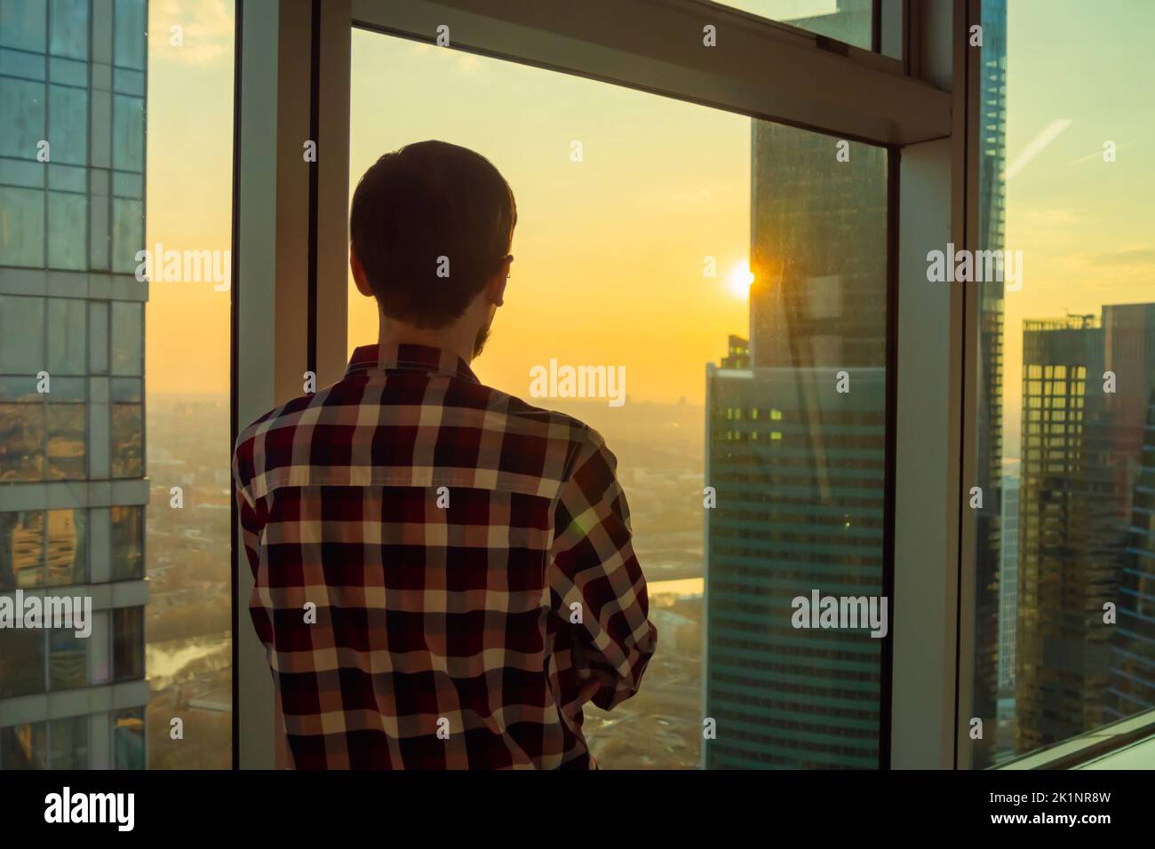 Vista posteriore dell'uomo che guarda il paesaggio urbano attraverso la finestra del grattacielo Foto Stock