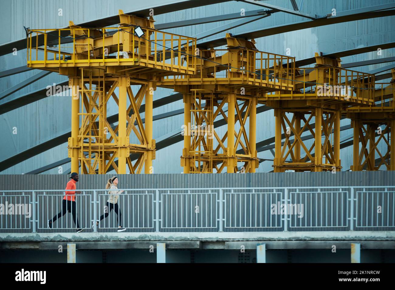 Fila di enormi costruzioni architettoniche in piedi lungo il ponte con due corridori che corrono lungo il fiume la mattina in ambiente urbano Foto Stock Fila di enormi costruzioni architettoniche in piedi lungo il ponte con due corridori che corrono lungo il fiume la mattina in ambiente urbano Foto Stock