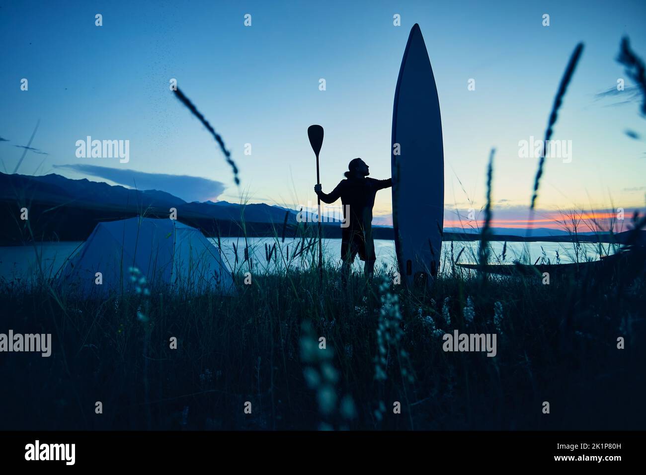Uomo in silhouette con pagaia e tavola SUP vicino tenda campeggio vicino al lago al tramonto in Kazakistan. Stand up paddle board attività ricreative all'aperto in Foto Stock