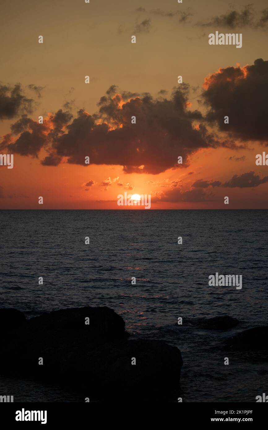 Sole che si staglia all'orizzonte. Tramonto dopo le rocce sulla spiaggia. Concetto di idea del mare o del paesaggio dell'oceano. Foto verticale. Nessuna gente, nessuno. Foto Stock
