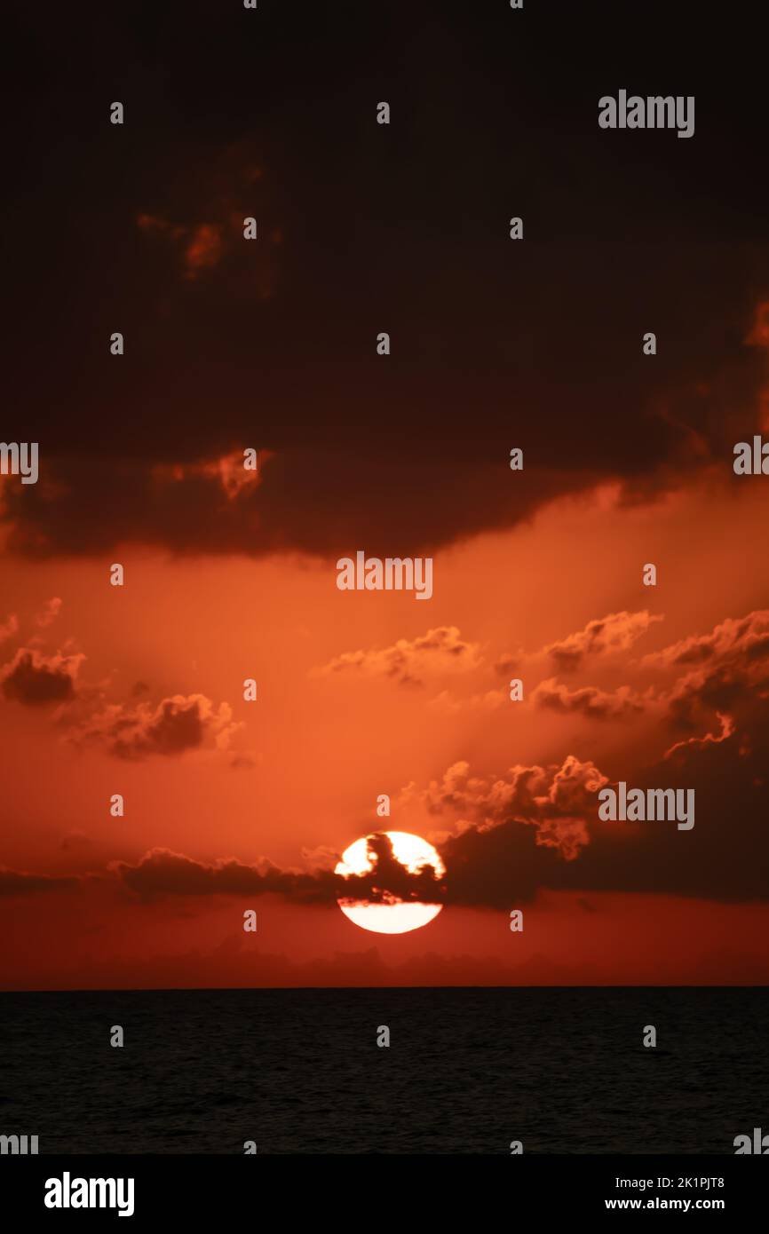 Vista verticale del tramonto. Il disco luminoso del sole è nascosto dietro le nuvole. Paesaggio arancione tramonto. Ore al crepuscolo. Rilassante, ambiente tranquillo idea. Foto Stock