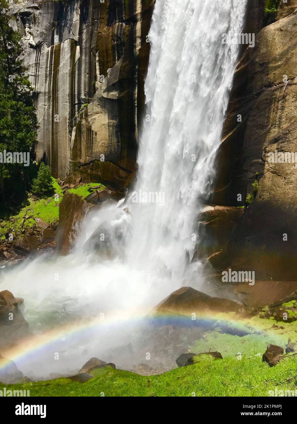 Un movimento verticale sfocato di una cascata che scorre in un lago con un piccolo arcobaleno tra le rocce Foto Stock
