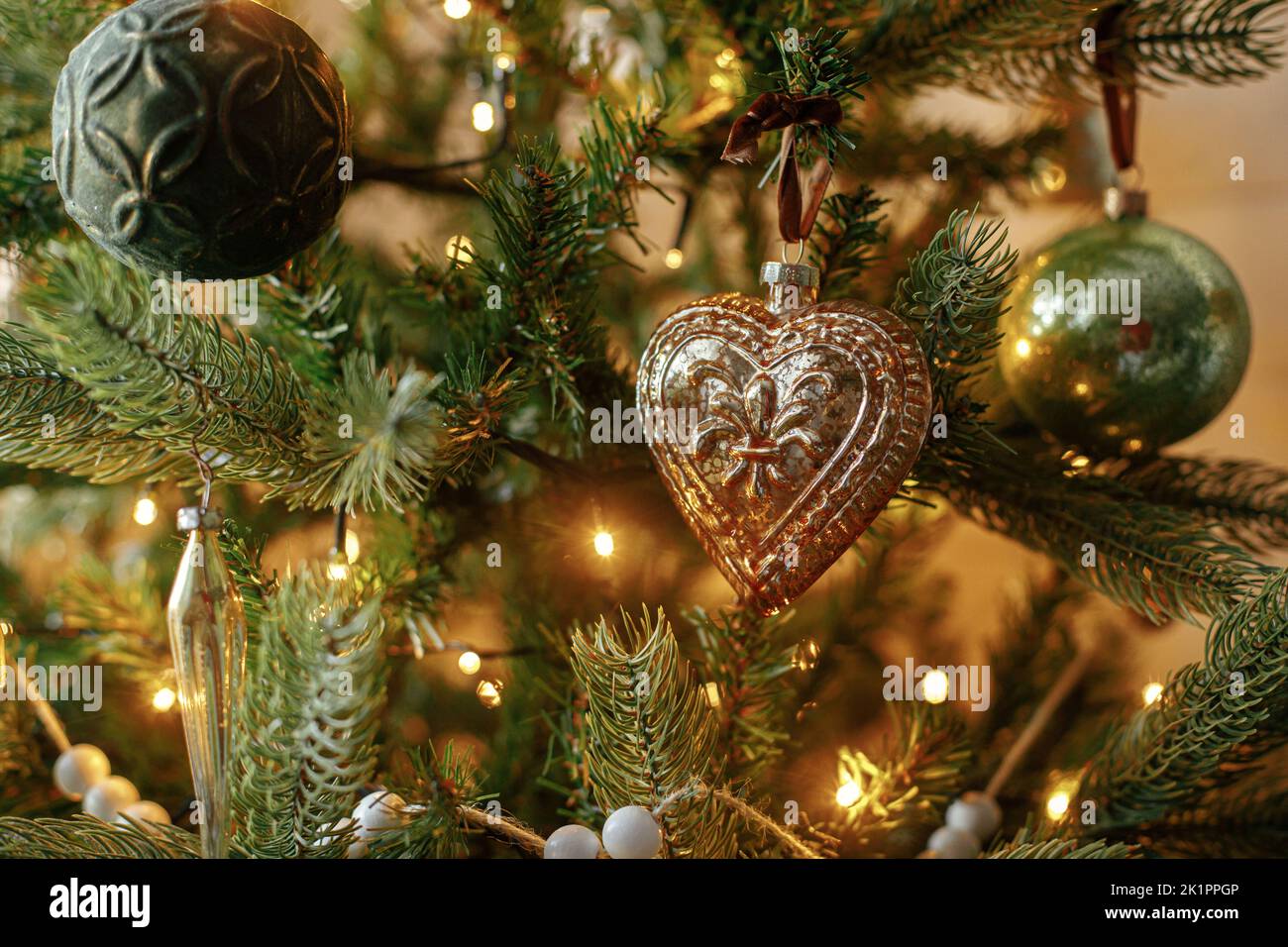 Albero di Natale con baubles vintage e luci dorate. Rami di albero di natale decorati in modo moderno con ornamenti eleganti vicino in una sala festiva. Vino Foto Stock