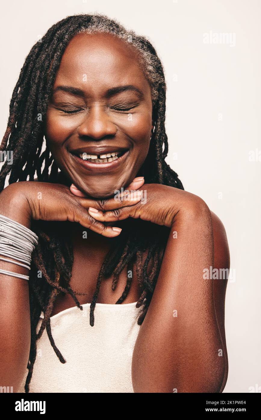 Donna felice sorridente con gli occhi chiusi su uno sfondo studio. Donna allegra con lucchetti spaventosi che indossano un asciugamano da bagno e un leggero make-up. Autoconfigurazione Foto Stock