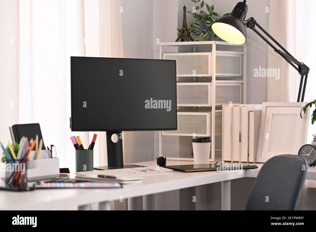 Uno schermo vuoto del calcolatore, cancelleria e lampada sul tavolo bianco in interno domestico moderno dell'ufficio Foto Stock