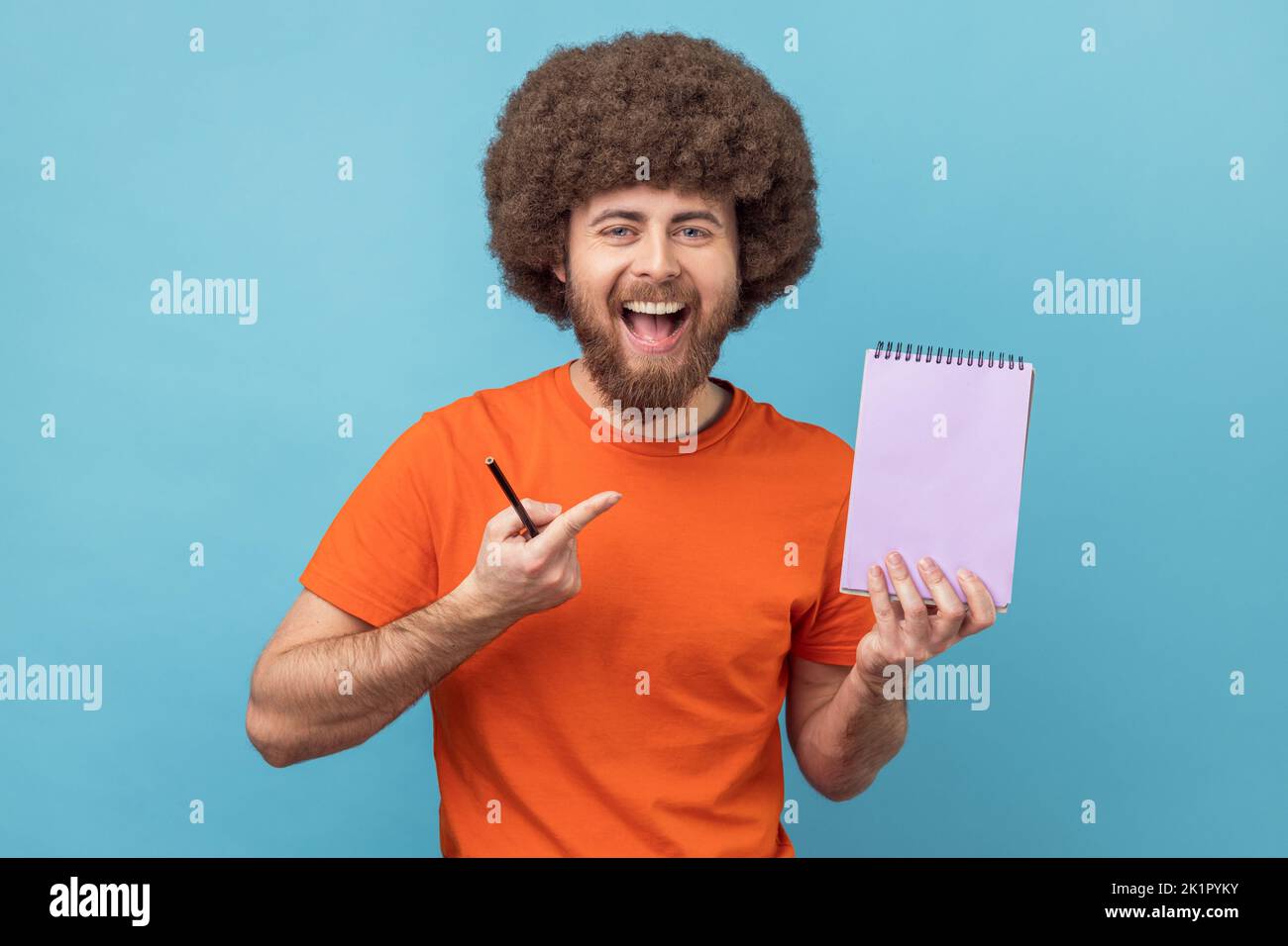 Scrivere l'elenco delle attività del promemoria nel notebook. Uomo con acconciatura afro mostrando pagina di carta vuota, modello mock up per idea creativa, testo pubblicitario. Studio in interni isolato su sfondo blu. Foto Stock