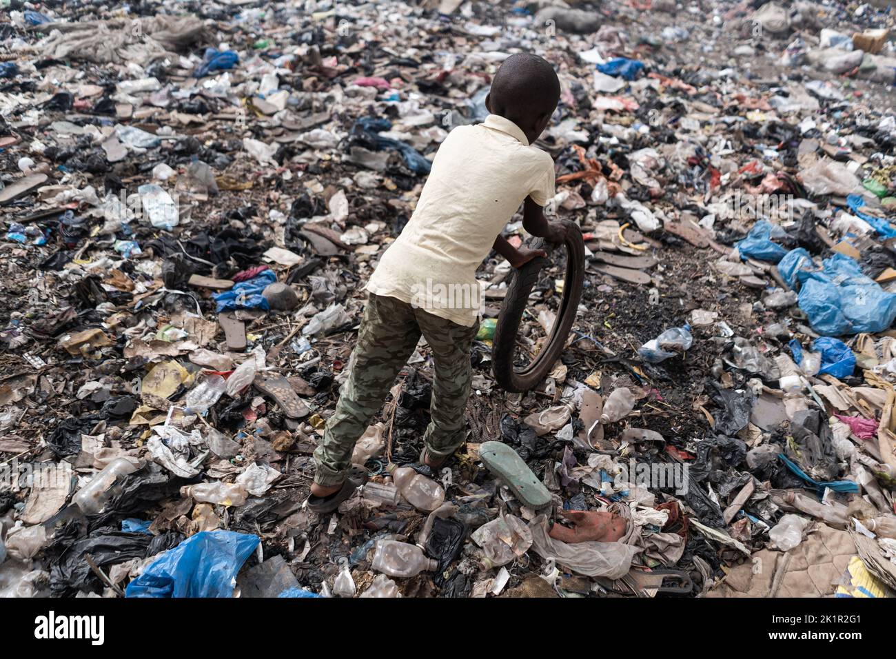 Vista dall'alto di un piccolo ragazzo africano che gioca con un vecchio pneumatico da bicicletta in una zona fortemente inquinata; simbolo dell'infanzia nei paesi sottosviluppati Foto Stock