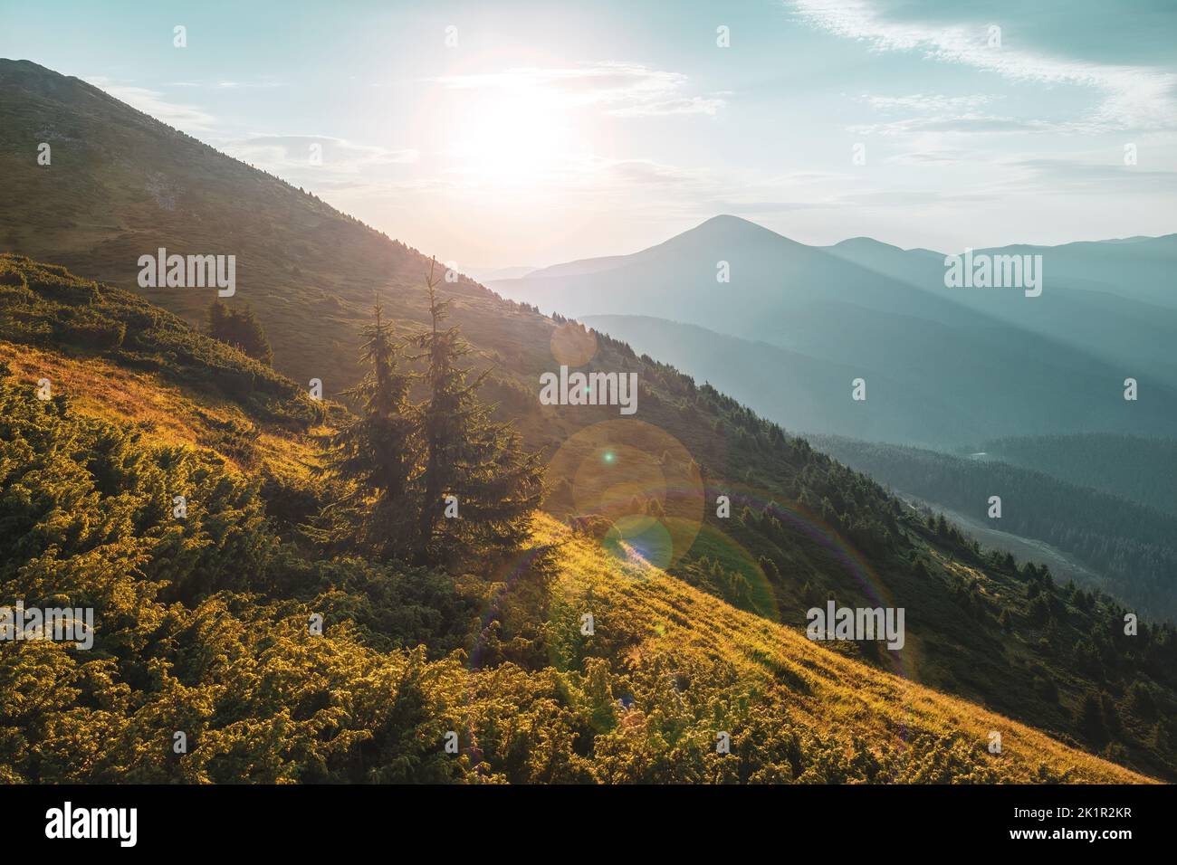 Bellissima alba in alto sulle montagne. Colline con lunghe ombre e primo piano illuminato dal sole che sorge. Foto Stock
