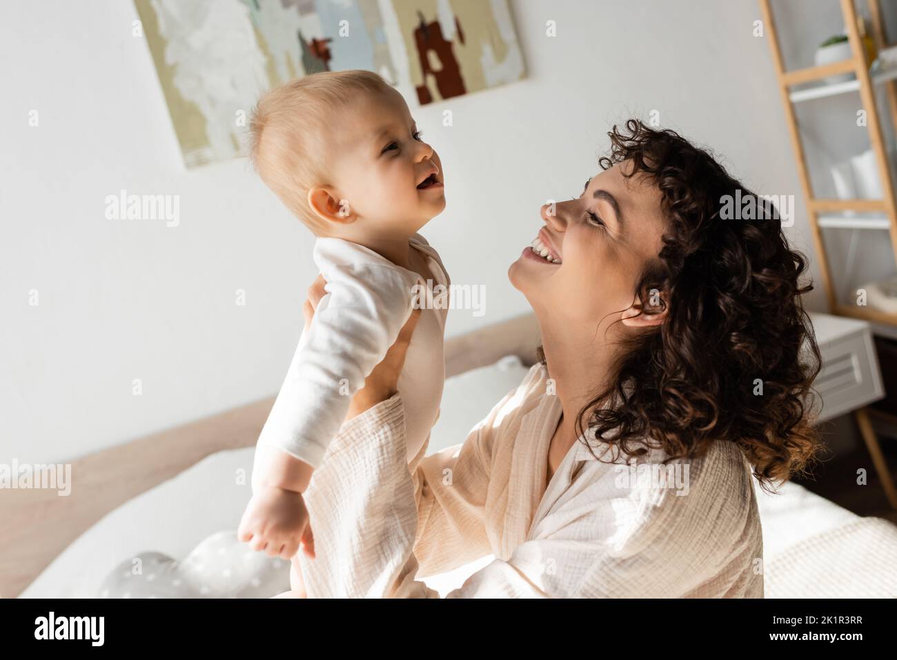 donna allegra e allegra in loungewear tenendo in braccio bambino figlia in romper, immagine di scorta Foto Stock