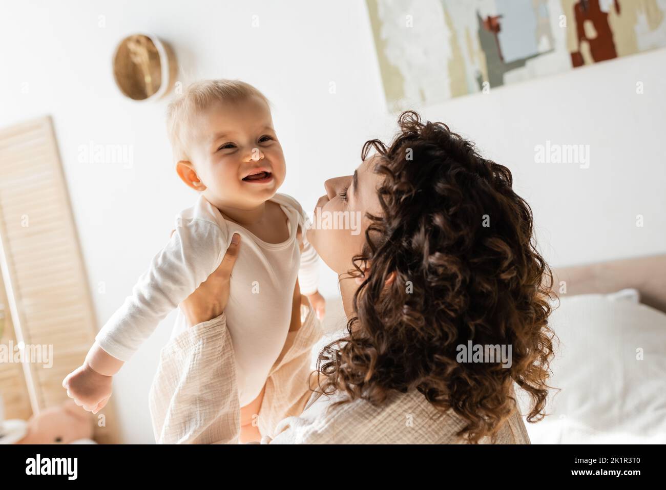 donna curly in loungewear tenendo in braccio bambino figlia in romper, immagine di scorta Foto Stock