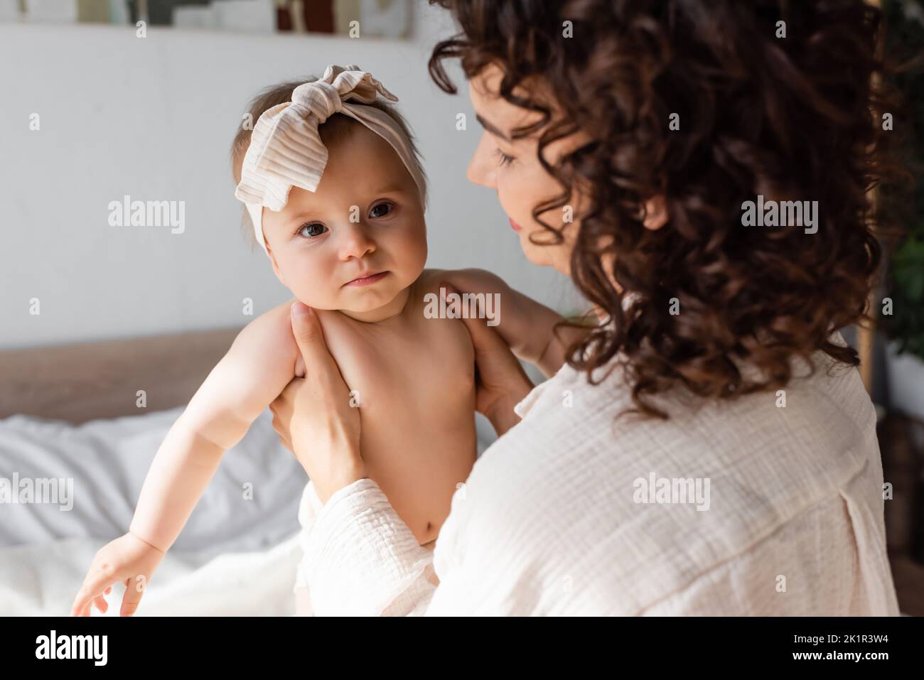 curly madre che tiene in braccio bambina in fascia con arco, immagine stock Foto Stock