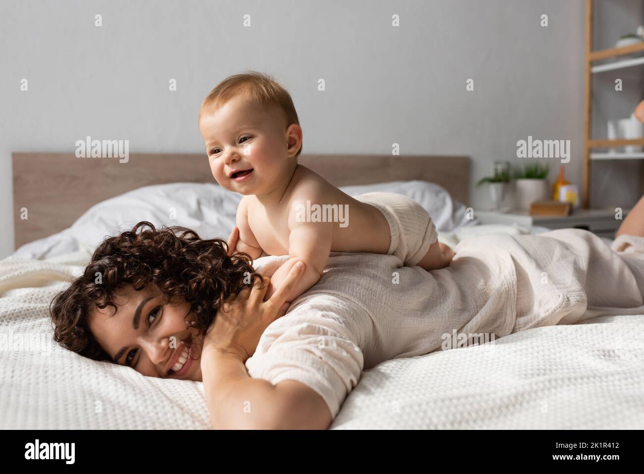 allegro bambino sdraiato sul retro di riccio e felice madre in camera da letto, immagine stock Foto Stock