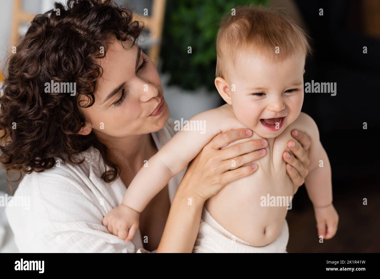 donna con capelli ricci tenendo in braccio bambino eccitato con bocca aperta, immagine stock Foto Stock